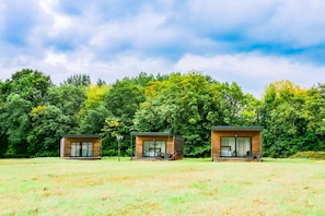 Three modern cabins with large windows, set in a grassy field with dense trees in the background. - Chateau Paradis - Twentyeight Bedroom Castle, Sleeps 91 (Benest)
