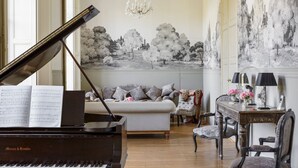 Un piano à queue, un canapé, une table à manger avec des chaises et un lustre dans une pièce bien éclairée, ornée d’une fresque murale.