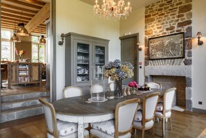 A dining area with a wooden table and chairs, a chandelier, a stone fireplace, and a view of the kitchen. - Chateau Quatre Saisons (Domjean)