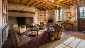 Un salon rustique avec des poutres apparentes, une cheminée, des sièges confortables et une vue dégagée grâce à de grandes fenêtres.