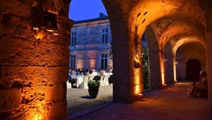 Une cour extérieure avec des arcades en pierre, un bâtiment en arrière-plan et des tables dressées pour le repas.