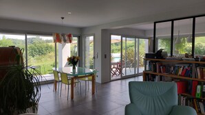 A spacious living area with a glass dining table, a teal armchair, and a bookshelf. - Beautiful, quiet Basque villa with heated pool (Ahetze)