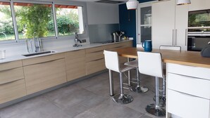 A modern kitchen with a large window, a wooden countertop, and a bar area with stools. - Beautiful, quiet Basque villa with heated pool (Ahetze)