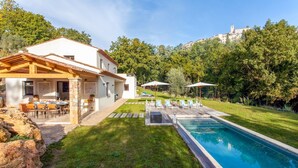 A modern villa with a swimming pool, outdoor seating, and a view of a hilltop town.