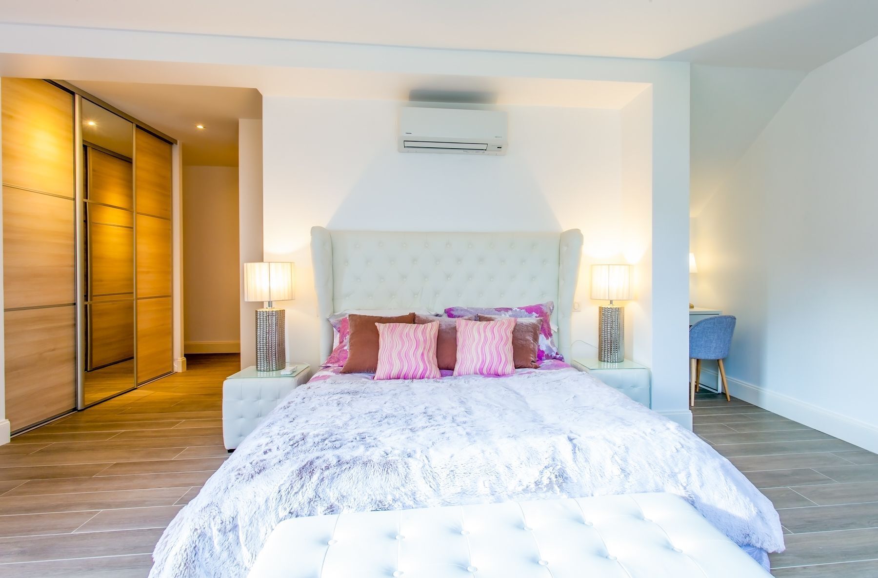 A bedroom with a large bed, two bedside tables with lamps, a wall-mounted air conditioner, and a sliding door closet.