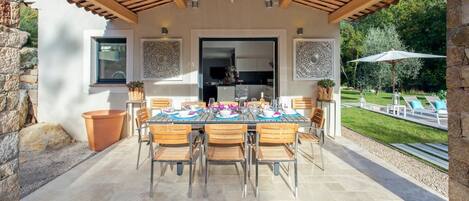 An outdoor patio with a table set for dining, surrounded by stone walls and a wooden pergola.