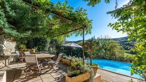 A patio with a wooden table and chairs, a pool, and surrounding greenery. - Le Jardin Secret - Four Bedroom Villa, Sleeps 8 (Laurac)
