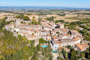 An aerial view of a village with traditional stone buildings, a central square, and surrounding fields.