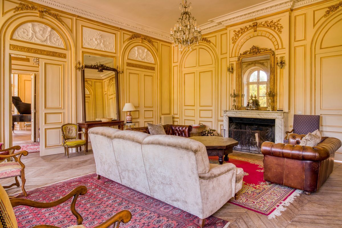 A grand room with a fireplace, a sofa, a leather armchair, and a chandelier.