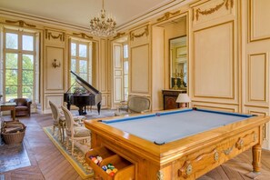 Una stanza con tavolo da biliardo, un pianoforte a coda e un biliardino.