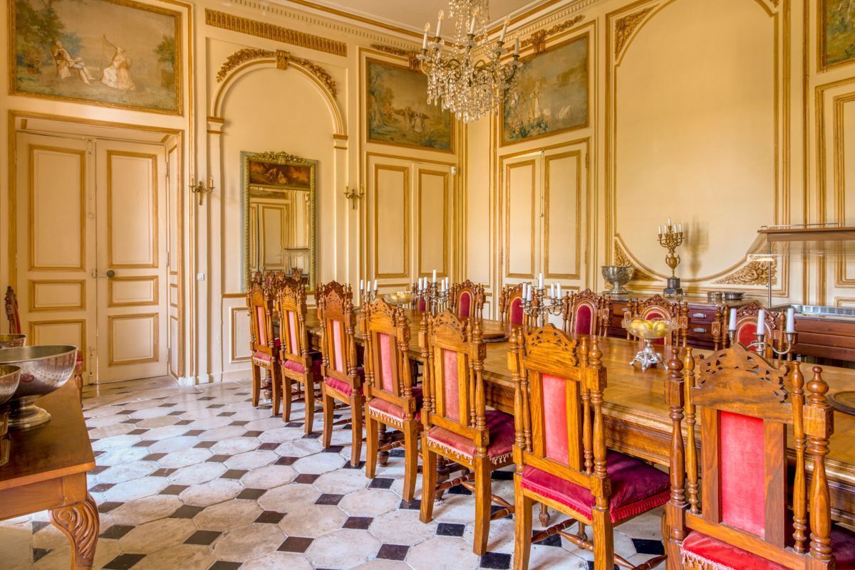 Een formele eetzaal met een lange tafel, versierde stoelen en een kroonluchter.