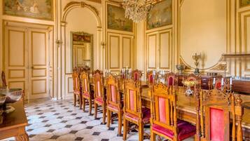 Een formele eetzaal met een lange tafel, versierde stoelen en een kroonluchter.