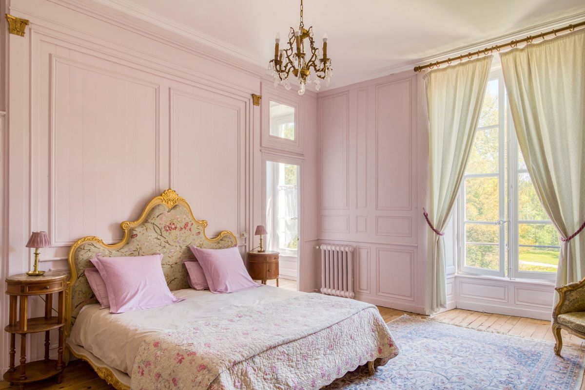 Un dormitorio con una cama grande, una araña, una ventana con cortinas y un radiador.