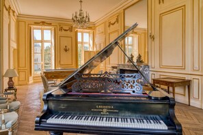 A grand piano in a spacious room with ornate wall paneling and a chandelier. - Chateau Des Temps - Ten Bedroom Castle, Sleeps 20 (Pleurs)