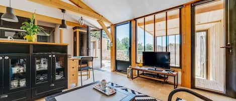 Amplia sala de estar con un televisor grande, vigas de madera y un ventanal corredero que da a un patio exterior.