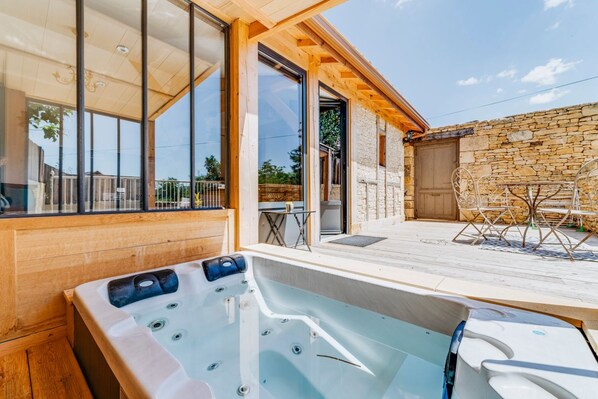 A wooden deck with a hot tub, stone wall, and outdoor seating area. - Gil’s Workshop - One Bedroom Villa, Sleeps 2 (Vézac)