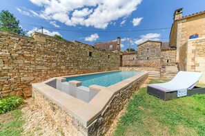 Une piscine bordée de pierres, dotée d’un espace salon intégré et d’une chaise longue.