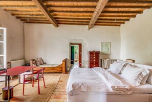 Una habitación con una cama, una mesa de madera, una silla, un radiador y una puerta que da a otra estancia.