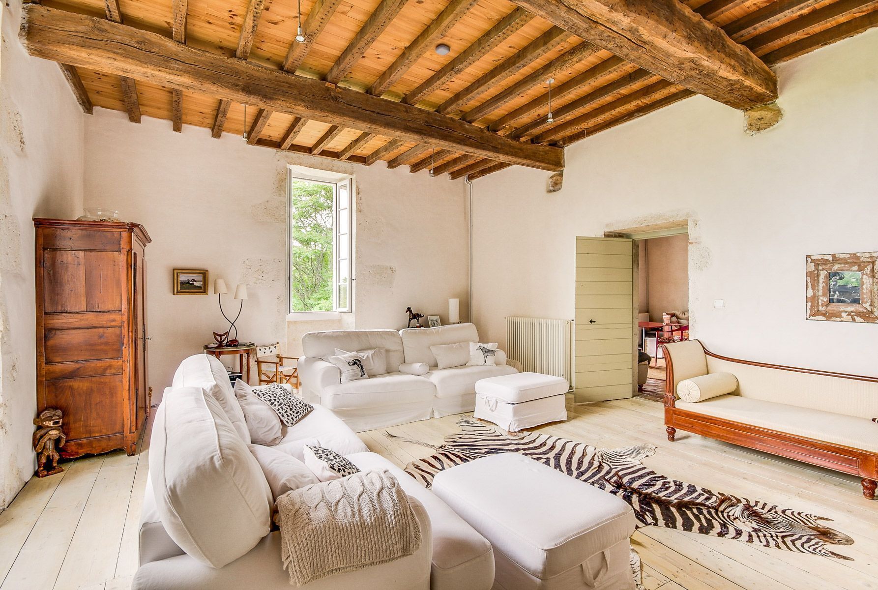 A spacious living room with a high wooden ceiling, white sofas, a zebra rug, and a wooden cabinet.