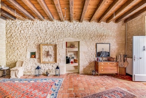 A rustic room with stone walls, wooden beams, a patterned rug, a dresser, and a mirror.