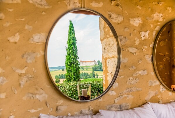A room with a round mirror reflecting a tall tree, a glass of water, and a building in the background.