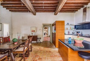 Una cocina rústica con vigas de madera a la vista, un comedor con sillas de madera y un piso de baldosas.