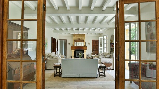 Un salon spacieux doté d’une cheminée, de poutres apparentes au plafond et d’une grande fenêtre.