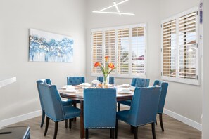 Une salle à manger avec une table ronde, des chaises recouvertes d’un tissu bleu et un vase rempli de fleurs.