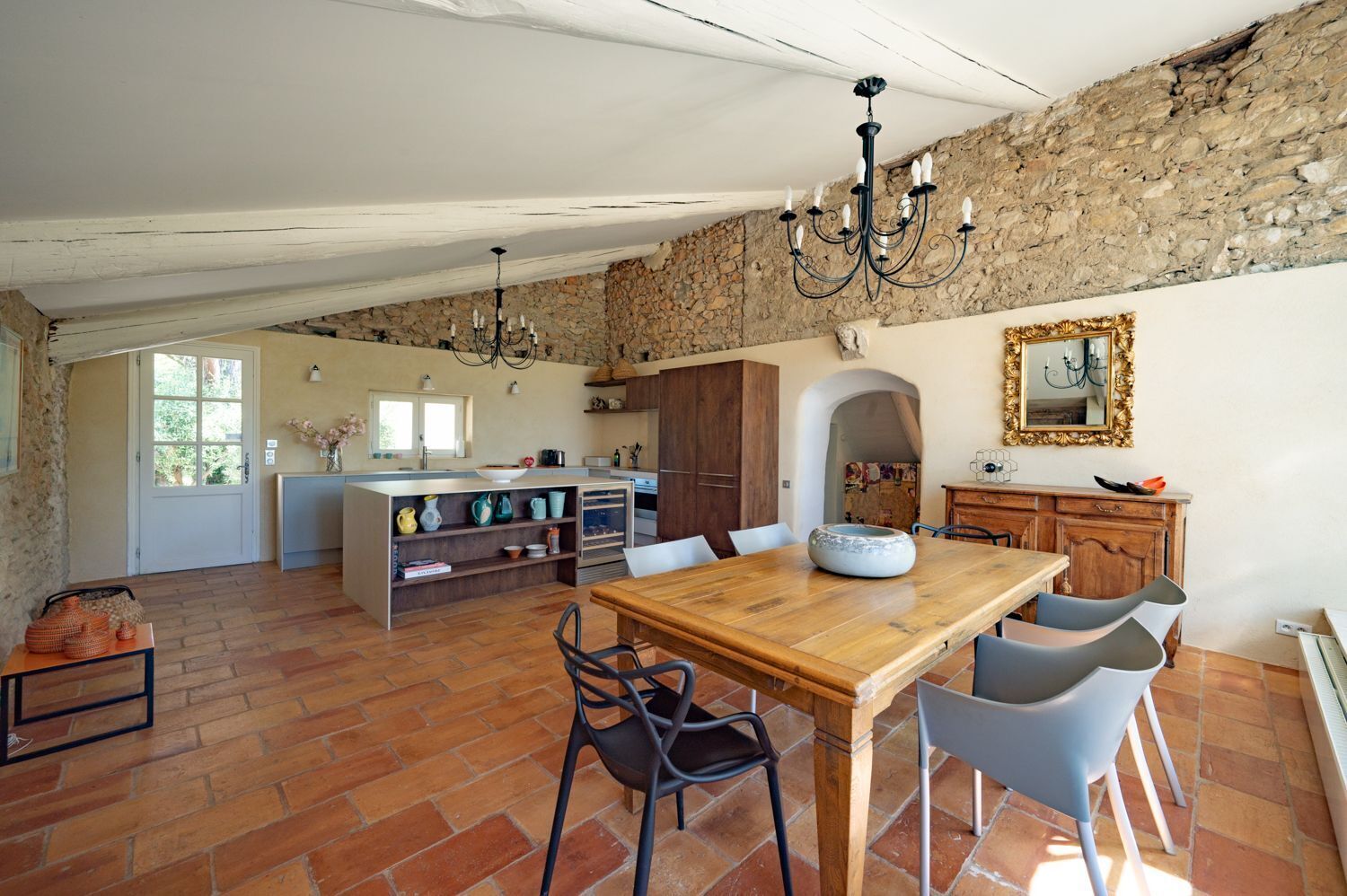 A spacious kitchen with a central island, a dining area with a wooden table and chairs, and a stone wall.