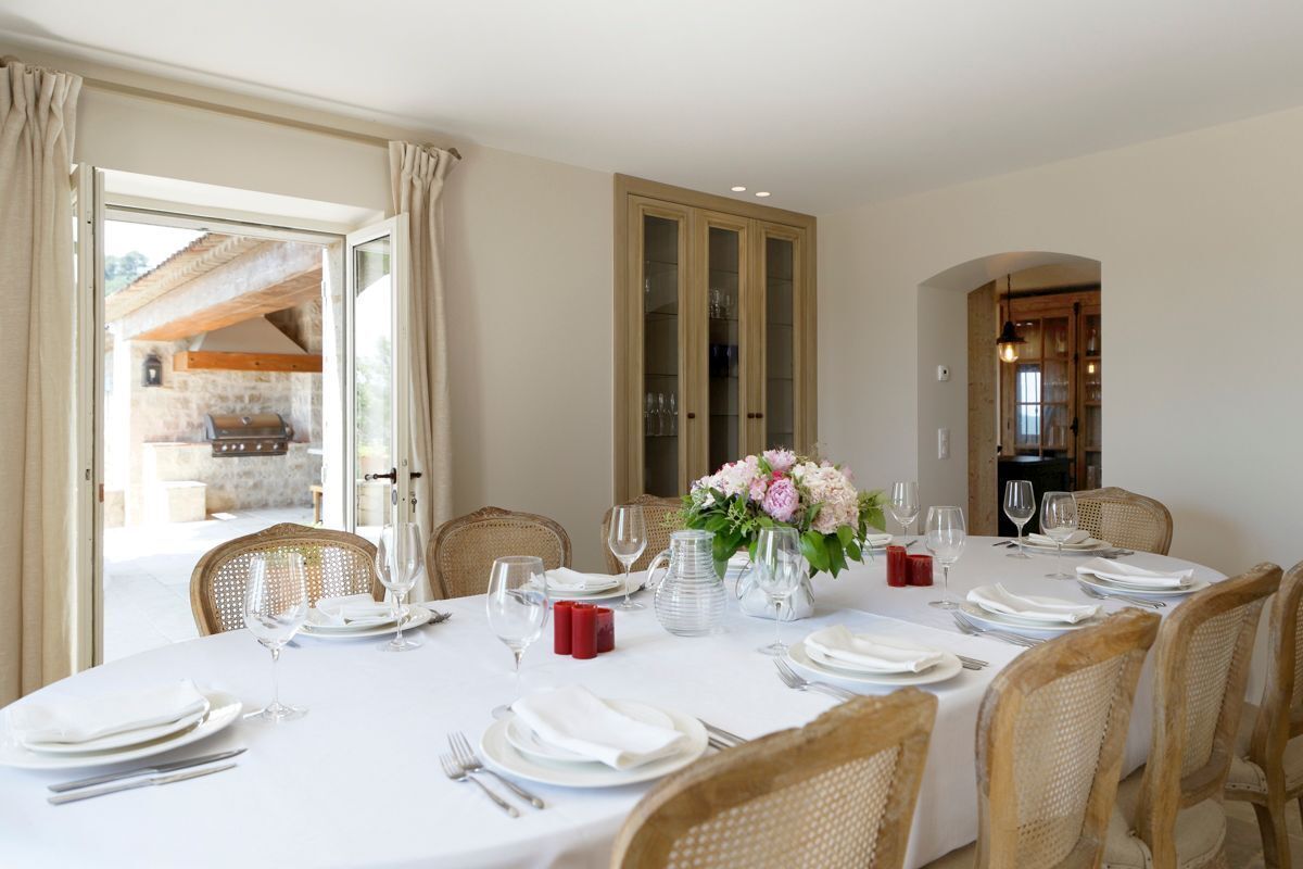 A dining area with a round table set for six, surrounded by wicker chairs.