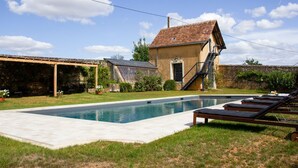 Une piscine avec des chaises longues, un petit bâtiment doté d’un escalier et un espace couvert agrémenté de plantes.