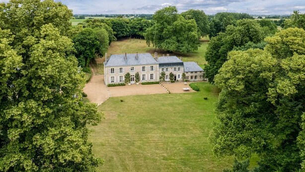 Un grand bâtiment historique, doté de plusieurs ailes, entouré d’une végétation luxuriante et d’une pelouse bien entretenue.
