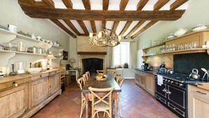Une cuisine rustique avec des poutres en bois, une cheminée et une table à manger avec des chaises.