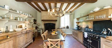 Una cocina rústica con vigas de madera, chimenea y una mesa de comedor con sillas.