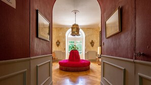 Un couloir avec un pouf rouge rond, un plancher en bois et un lustre.