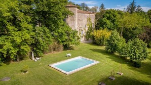 Une piscine rectangulaire entourée d’une pelouse bien entretenue, avec un bâtiment en pierre en arrière-plan.