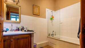 A bathroom with a wooden vanity, a white sink, a mirror, a shower with a glass door, and a yellow bath mat. - Cottage Des Cathares (Plaigne)