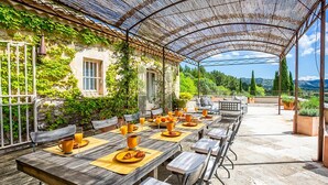 Ein Essbereich im Freien mit Tischen und Stühlen, einer Pergola und Blick auf die umliegende Landschaft.