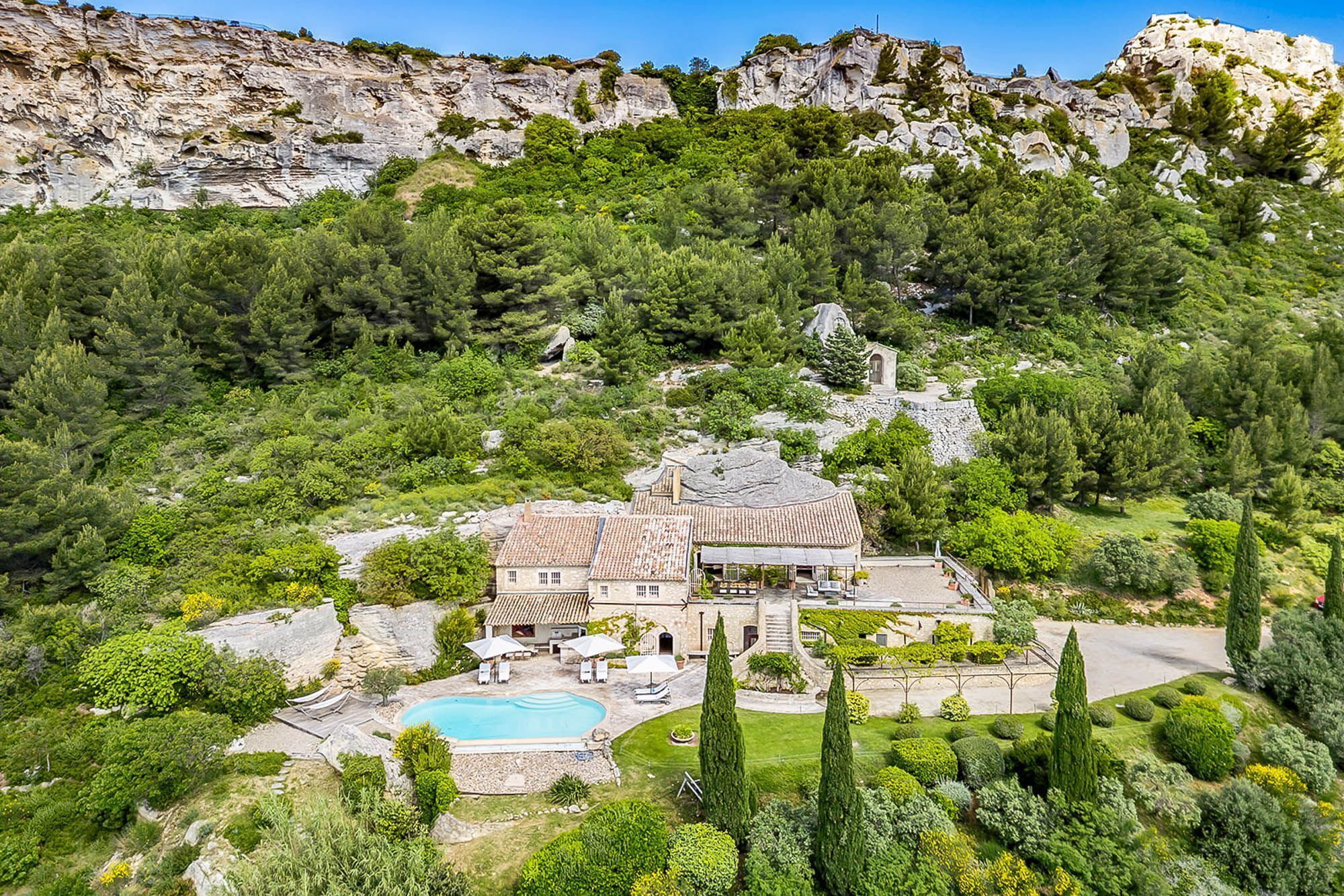 A large house with a swimming pool, surrounded by lush greenery and rocky cliffs.