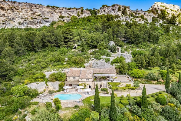 Une grande maison avec une piscine, entourée d’une végétation luxuriante et de falaises rocheuses.