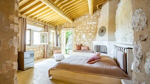 Ein Schlafzimmer mit Steinsandsteinwand, einem Bett mit Quilzdecke, einer weißen Kommode und einem Fenster mit Vorhängen.