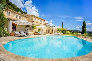 A pool area with lounge chairs and umbrellas, surrounded by stone buildings and greenery. - Les Rochers - Five Bedroom Villa, Sleeps 10 (Les Baux de Provence)
