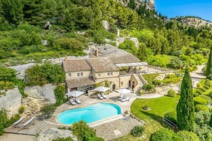 A stone villa with a swimming pool, surrounded by lush greenery and a mountainous backdrop.