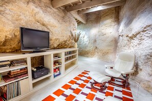 A room with a television on a shelf, a white chair, and a patterned rug.