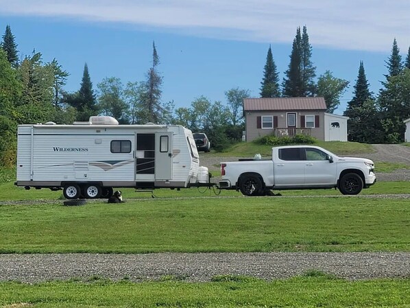 A white truck towing a white recreational trailer with the brand name 'Wilderness' visible on the side.