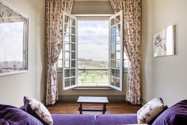 A room with a view through an open window, a wooden bench, and purple upholstered furniture. - Manoir Des Chasseurs (Saint-Prix)