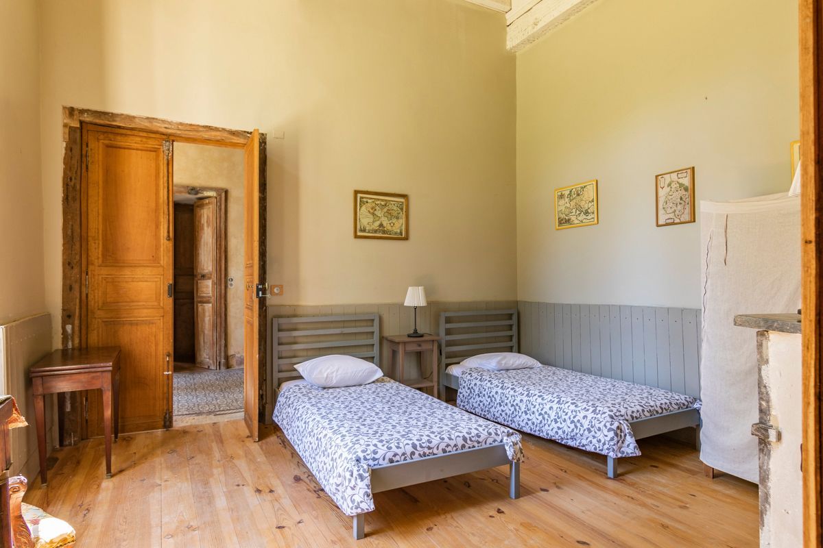 Una habitación con dos camas individuales, una puerta de madera, una mesita y una lámpara.