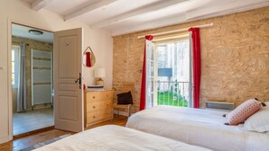 Ein Schlafzimmer mit zwei Betten, einer Steinwand, einem Fenster mit roten Vorhängen und einer Tür, die auf einen Balkon führt.