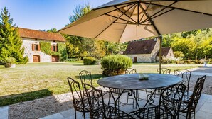 An outdoor patio with a round table and chairs, a large umbrella, and a stone building in the background. - Manoir 1731 - Six Bedroom Villa, Sleeps 12 (Carlux)