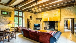 A rustic living room with exposed wooden beams, a stone fireplace, a television, and a cozy seating area. - Manoir 1731 - Six Bedroom Villa, Sleeps 12 (Carlux)